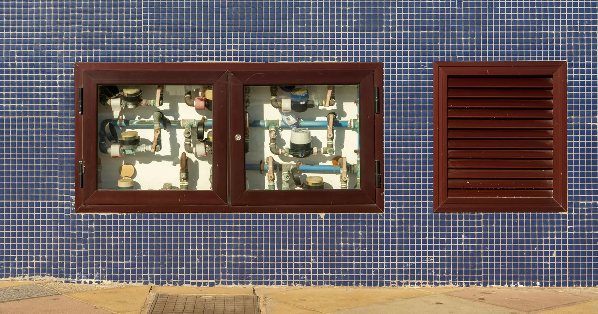Close-up of a tiled wall with exposed water meters and vent in Arinaga, Spain.