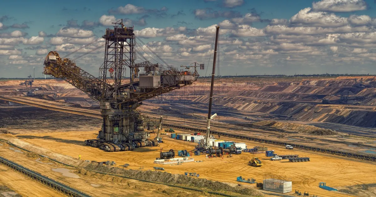 Aerial view of heavy machinery operating in a vast open-pit mine under a cloudy sky.