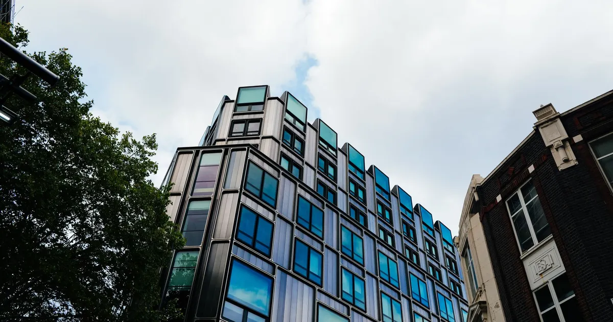 A contemporary building with reflective windows in an urban setting under a cloudy sky.